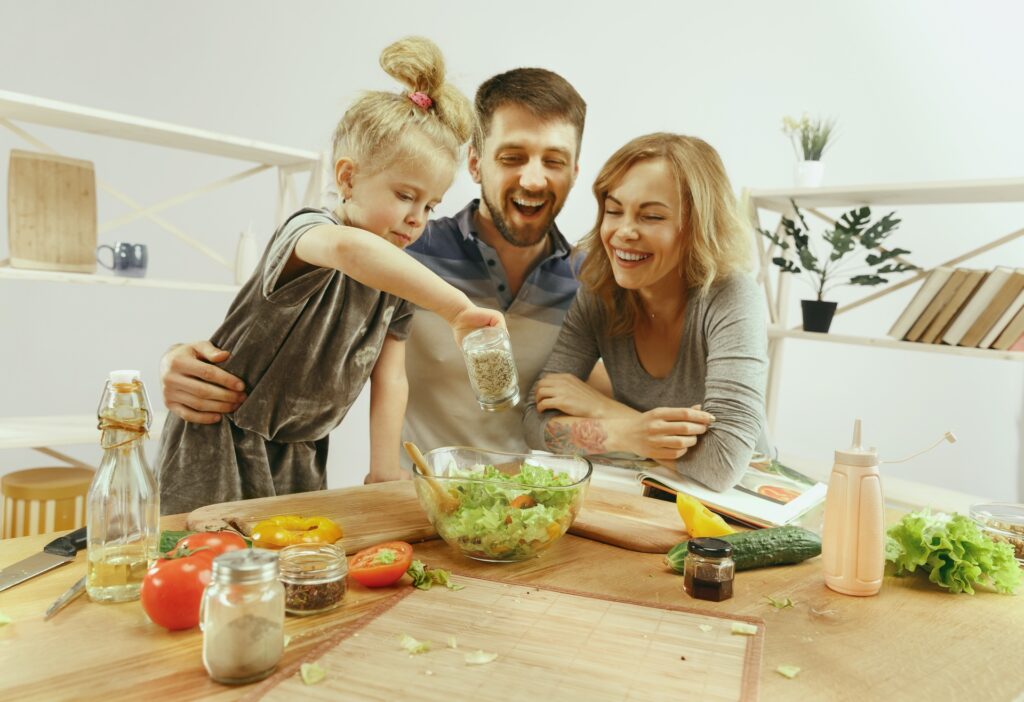 cute-little-girl-her-beautiful-parents-are-cutting-vegetables-smiling-while-making-salad-kitchen-home
