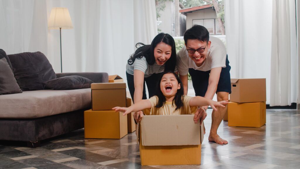 happy-asian-young-family-having-fun-laughing-moving-into-new-home-japanese-parents-mother-father-smiling-helping-excited-little-girl-riding-sitting-cardboard-box-new-property-relocation